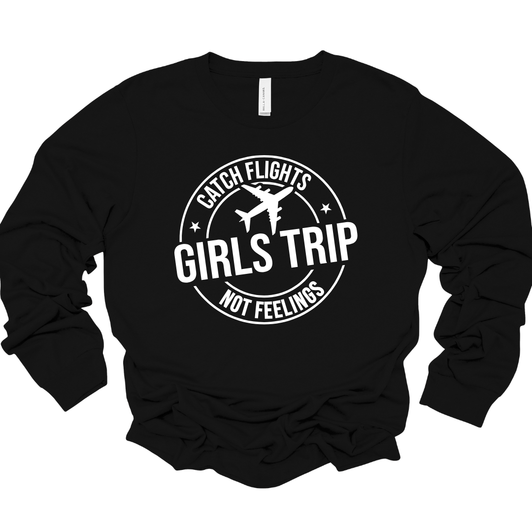 Black unisex long sleeve shirt with white “Girls Trip Catch Flights Not Feelings” circular design and airplane graphic.